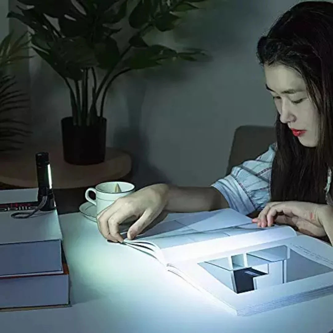 Person reading a book illuminated by a small lamp in a dimly lit room.