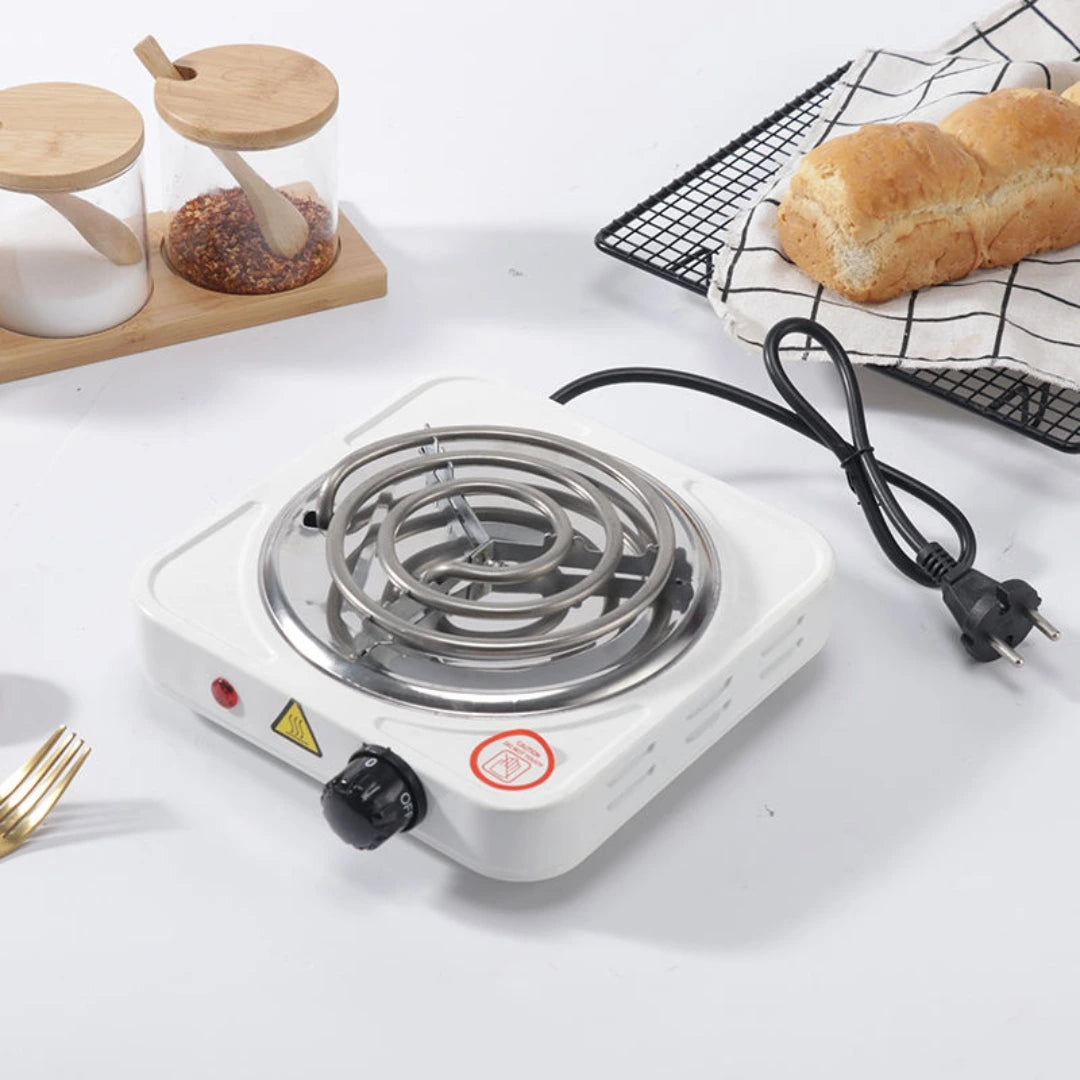 Single burner electric stove on a white surface with bread and a cooling rack in the background.
