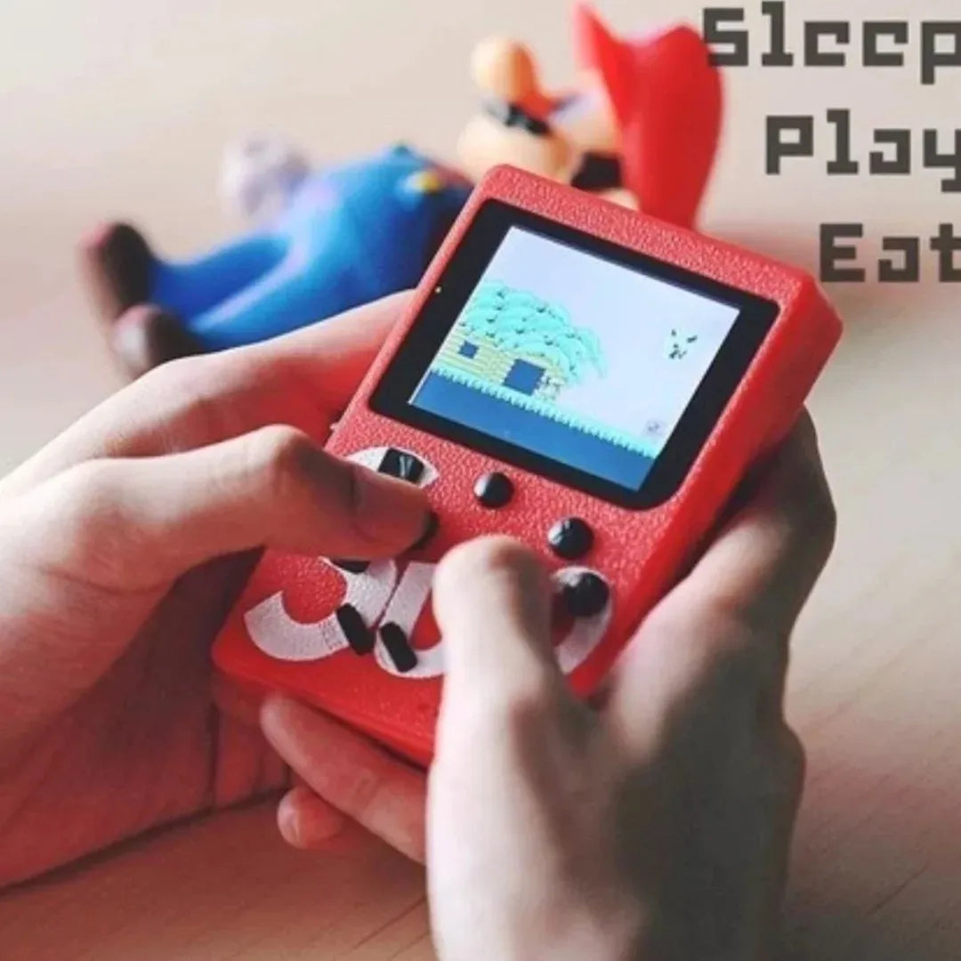 Red handheld gaming console with a game displayed, held by hands on a wooden surface with toys in the background.