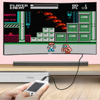 Hand holding a handheld gaming device connected to a TV displaying a retro video game.