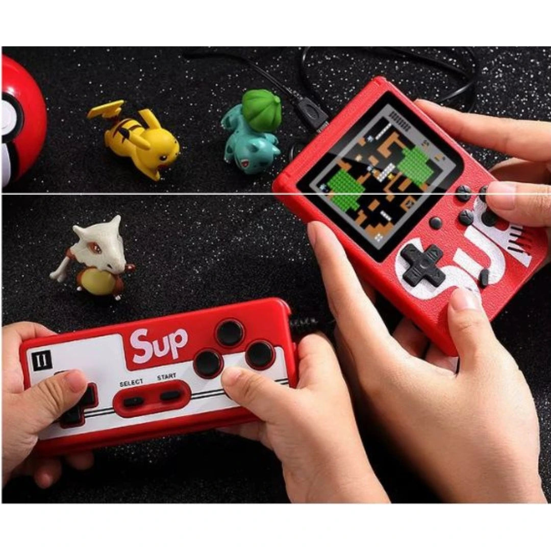 Two handheld gaming consoles with 'Sup' branding, held by hands, on a dark surface with small figurines.